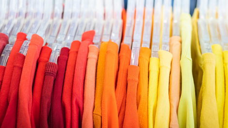 Orange, red and yellow shirts on a clothes rail.